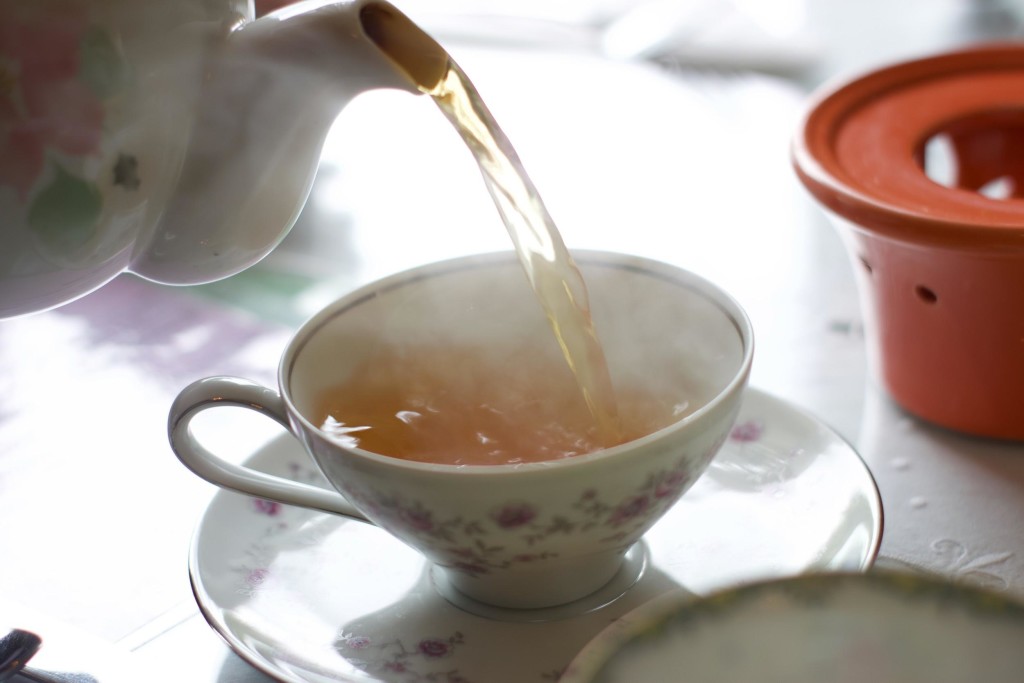 person pouring tea on white teacup