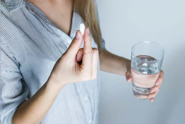Woman Holding Half-full Glass and White Medicine Pill