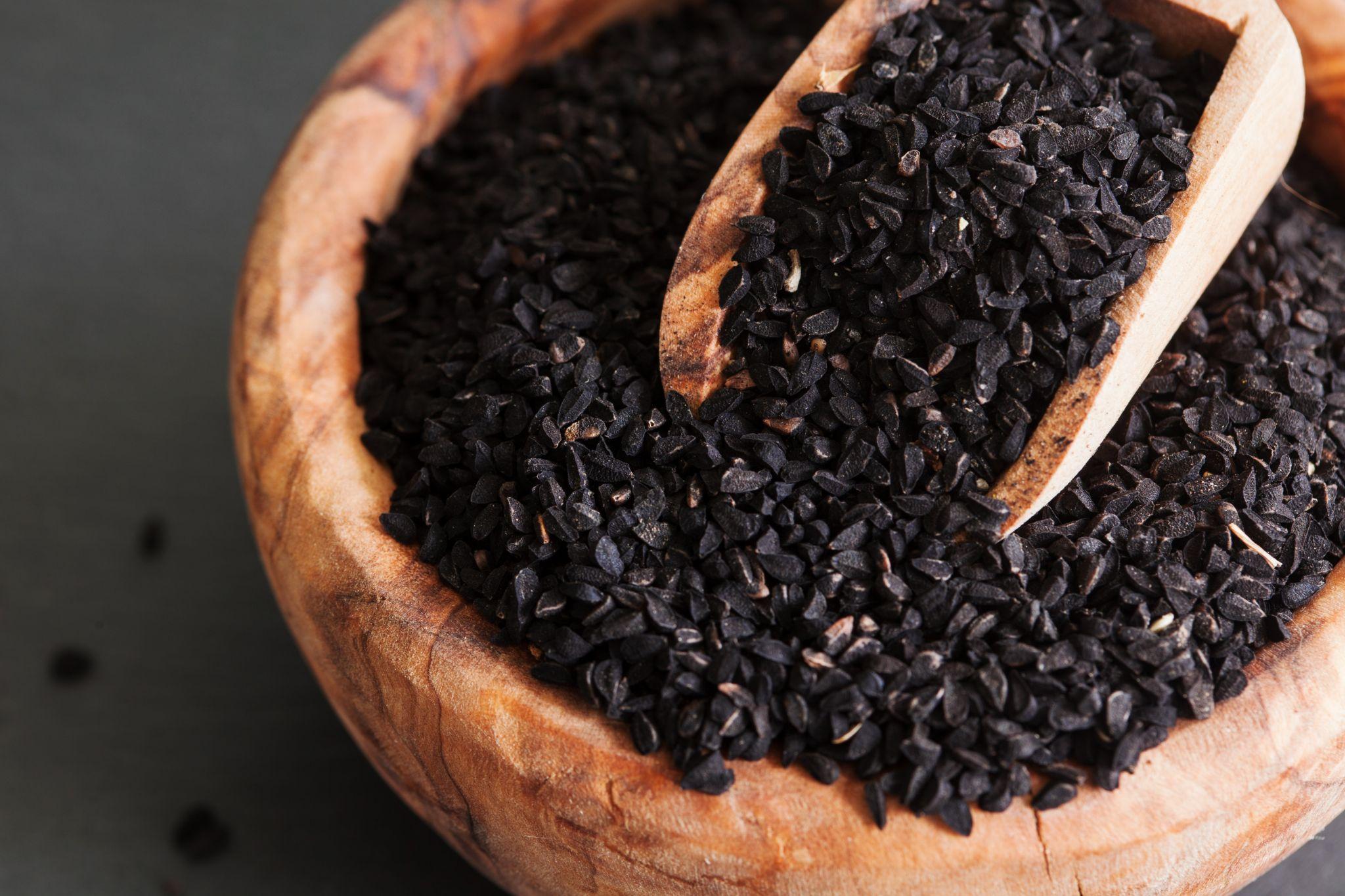 Black cumin seeds in bowl with spoon on black slate background